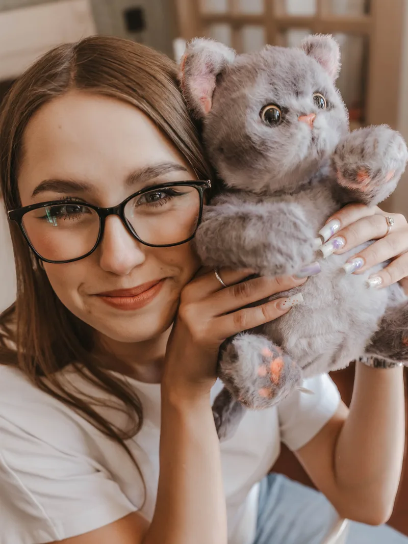 Девушка в очках прижимает к щеке плюшевого дымчатого кота